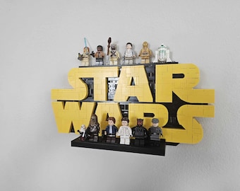 May include: A yellow "STAR WARS" sign made of Lego bricks, with various Lego Star Wars characters displayed on a black shelf. The sign is mounted on a white wall. The characters include Darth Maul, Chewbacca, and R2-D2.