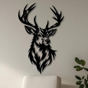 Pode incluir: Arte de parede de cabeça de veado em metal preto. A cabeça do veado é uma silhueta com chifres e pêlo detalhados. A arte de parede é montada numa parede branca acima de uma poltrona branca e uma planta em vaso. O texto "HELYA WALL ART" é visível.