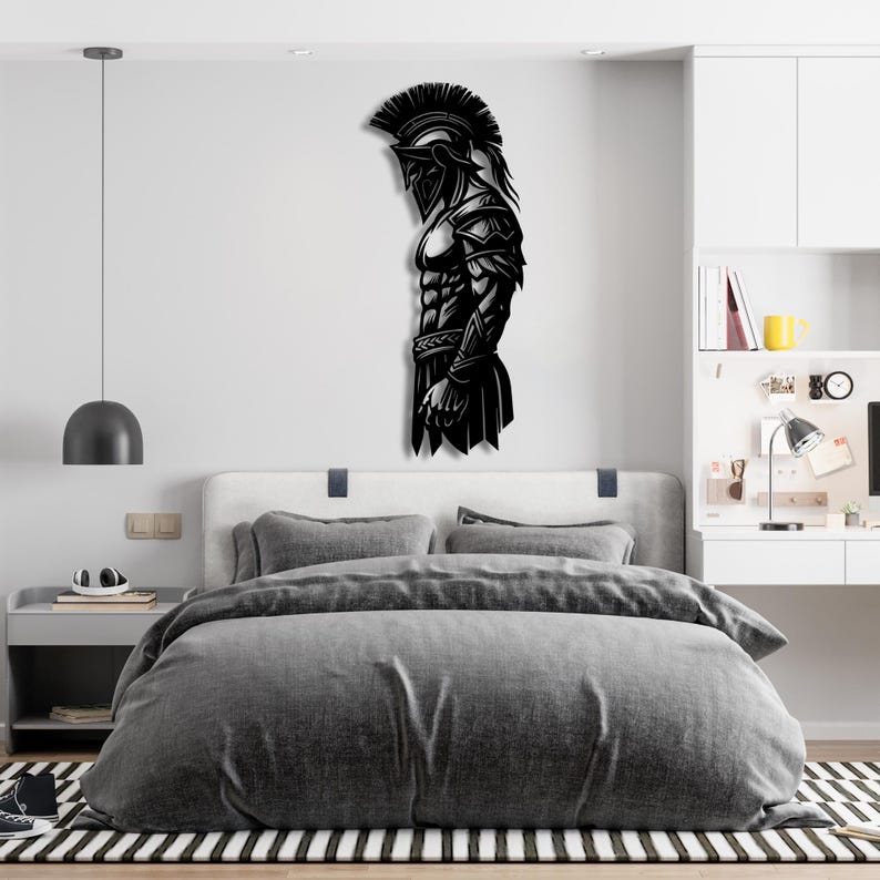 May include: Black metal wall art depicting a Spartan warrior in profile. The artwork features intricate details of the warrior's helmet, armor, and physique. The piece is mounted on a white wall above a bed with gray bedding, creating a striking contrast.