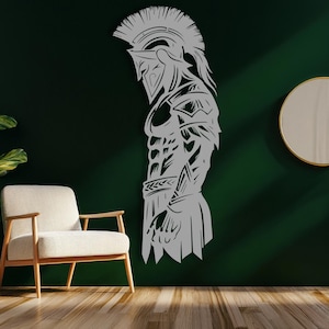 May include: A gray metal wall art piece depicting a Spartan warrior in profile. The artwork features intricate details of the warrior's helmet, armor, and physique. The piece is mounted on a dark green wall, with a chair and mirror in the background.