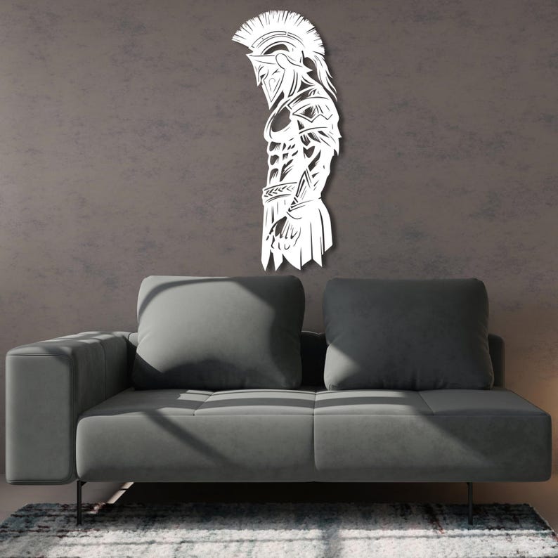 May include: White metal wall art depicting a Spartan warrior in profile. The artwork features a detailed design of the warrior's helmet, armor, and physique. The art is mounted on a gray wall above a gray sofa.