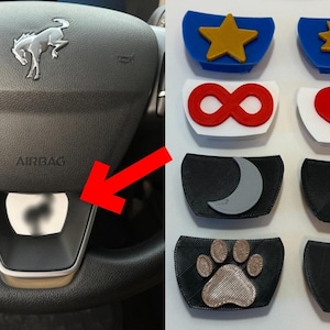 May include: A car steering wheel with a silver horse emblem. Beside it are several decorative car accessories with designs such as a gold star, a red infinity symbol, and a silver paw print.