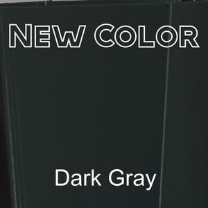 Op de afbeelding: Een effen donkergrijs oppervlak met de tekst NEW COLOR in wit omrande hoofdletters bovenaan en de tekst Dark Gray in een wit schreefloos lettertype in het midden eronder, wat een nieuwe kleuroptie voor een product of materiaal aangeeft.