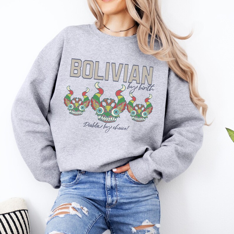 May include: Gray sweatshirt with a graphic print of three colorful cartoon creatures with the text "Bolivian by birth, Diablo by choice!"