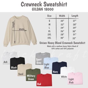May include: A beige crewneck sweatshirt with size and width measurements in inches. The sweatshirt is available in 10 colors: ash, black, sport grey, light blue, navy, white, sand, military green, red, and light pink.