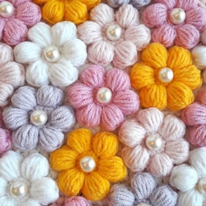 Puede incluir: Primer plano de una tela de crochet con un patrón de flores. Las flores están hechas de hilo de diferentes colores, incluyendo rosa, blanco, amarillo y morado. Cada flor tiene una perla en el centro.
