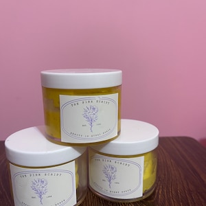 May include: Three white jars with yellow contents and labels that read "The Pink Script Est. 1990 Beauty in Every Shade".