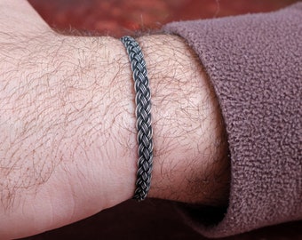 Könnte beinhalten: Ein geflochtenes Armband aus Silber am Handgelenk einer Person.