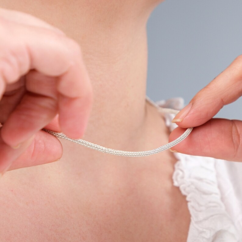 K&ouml;nnte beinhalten: Nahaufnahme einer silbernen Kettenkette, die um den Hals einer Person getragen wird. Die Kette ist d&uuml;nn und zart, mit einem schlichten Design.