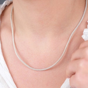 K&ouml;nnte beinhalten: Eine silberne Kettenkette mit einem zarten, gewebten Design. Die Kette ist d&uuml;nn und hat einen dezenten Schimmer.