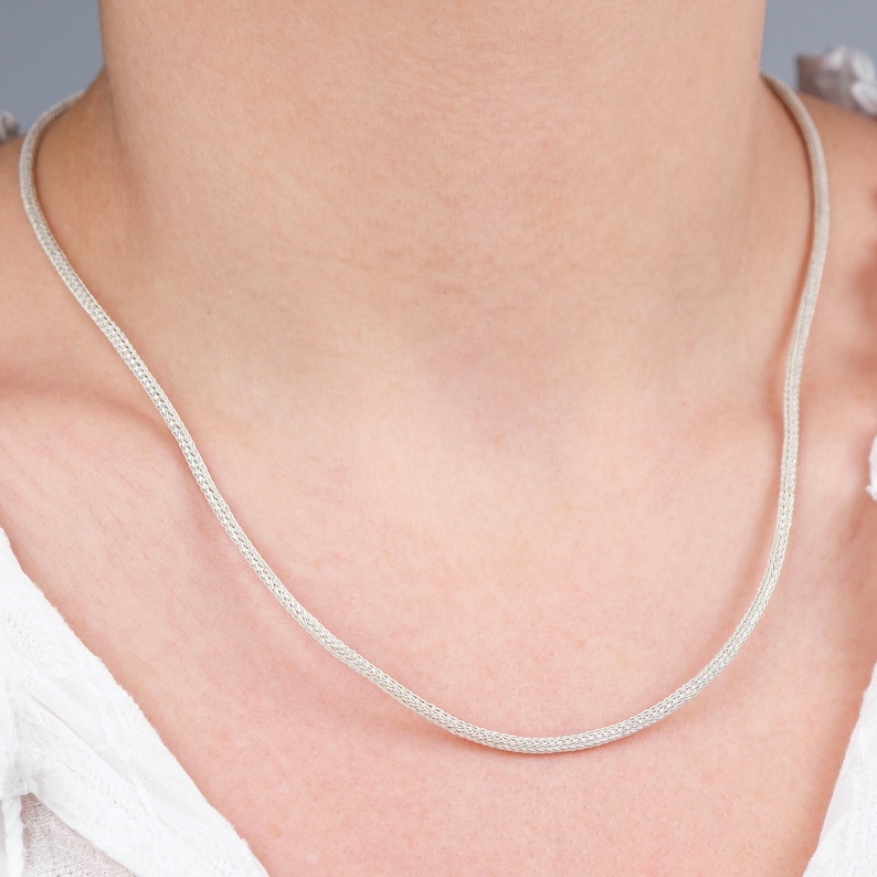 K&ouml;nnte beinhalten: Eine silberne Kettenkette mit einem zarten, gewebten Design.