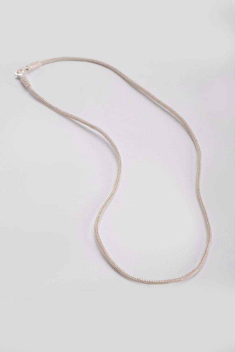 K&ouml;nnte beinhalten: Eine silberne Kettenkette mit einem zarten, geflochtenen Design. Die Kette ist etwa 45 cm lang.