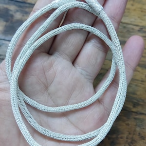 May include: A silver chain necklace with a braided design. The chain is coiled and laid out on a hand.