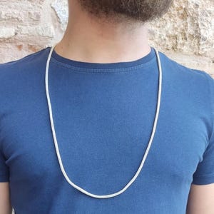 May include: A silver chain necklace on a person wearing a blue t-shirt.