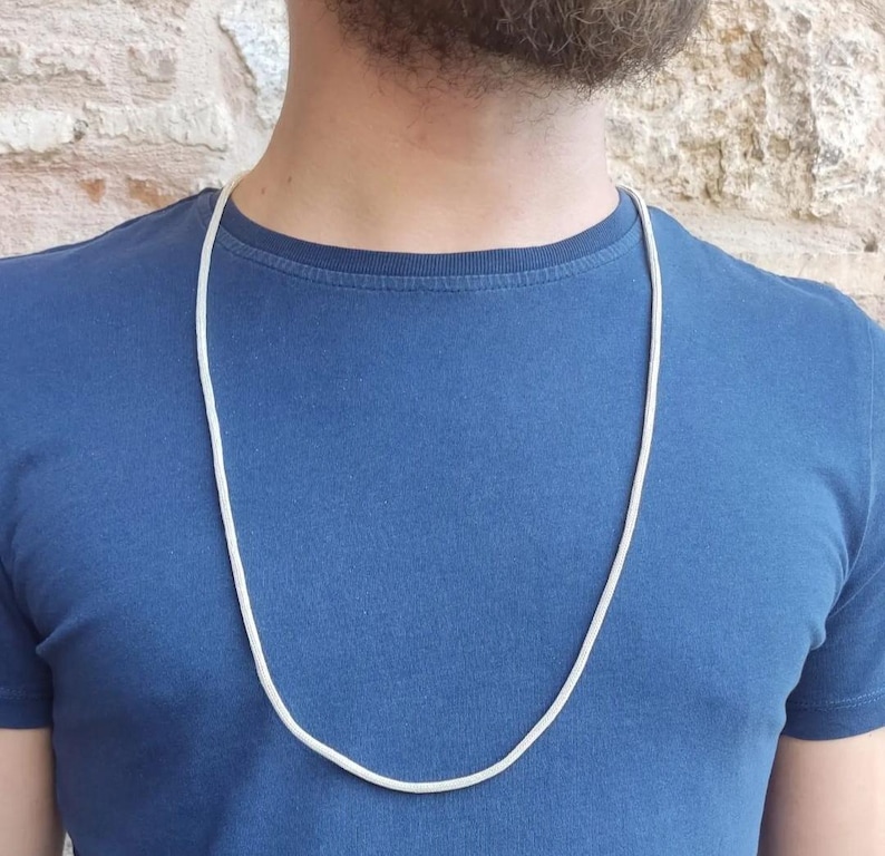 May include: A silver chain necklace on a person wearing a blue t-shirt.