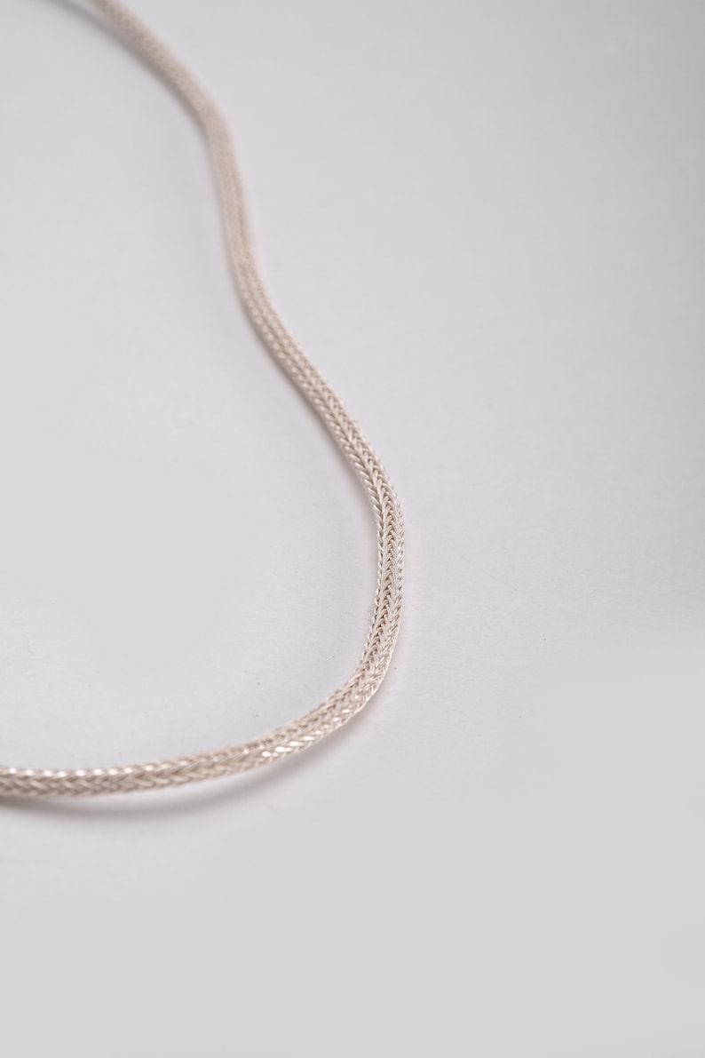 K&ouml;nnte beinhalten: Eine silberne Kettenkette mit geflochtenem Design.