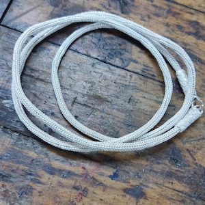 May include: A silver chain necklace with a braided design. The chain is lying on a wooden surface.