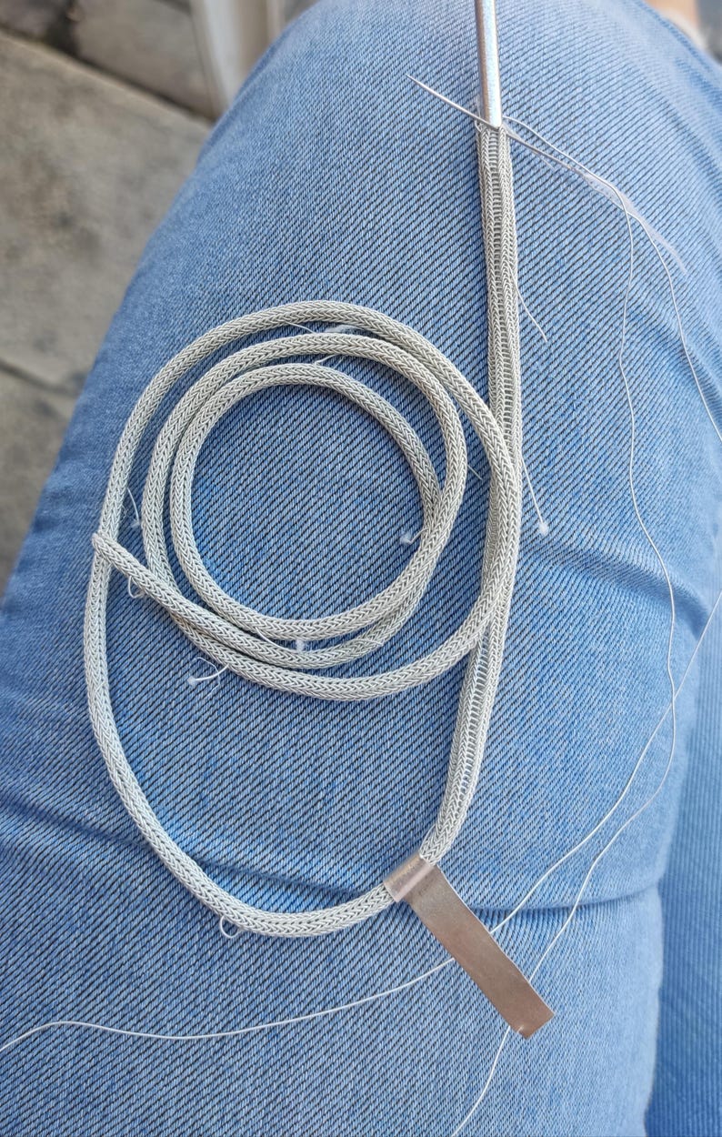 May include: A silver chainmail necklace with a silver metal clasp. The chainmail is made of small, interconnected metal rings.