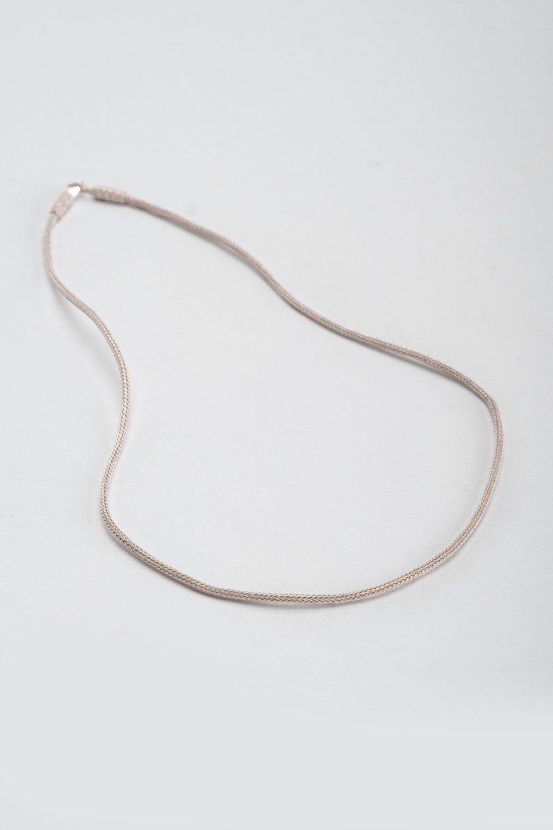 K&ouml;nnte beinhalten: Eine silberne Kettenkette mit einem zarten, gewebten Design.
