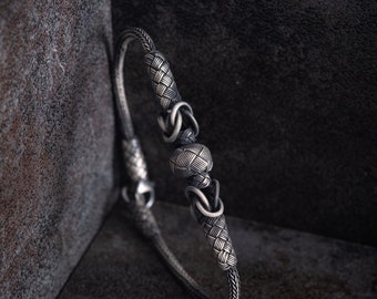 May include: A silver bracelet with a woven design and a round, textured bead in the center.
