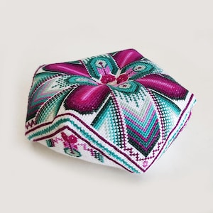May include: A square, handmade cushion with a vibrant, geometric design. The cushion features a central floral pattern in shades of magenta and teal, surrounded by white and purple accents. The edges are finished with a detailed border.