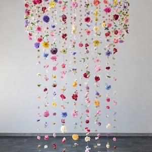 Peut inclure: Une installation florale composée d'une multitude de fleurs colorées suspendues à un cadre circulaire. Les fleurs, dans des tons de rouge, rose, jaune et violet, pendent à différentes longueurs, créant un affichage visuellement saisissant. L'arrangement est sur fond neutre.