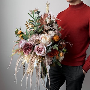 May include: A large, colorful bouquet featuring roses, hydrangeas, and other flowers in shades of pink, peach, and cream. The arrangement includes greenery and decorative elements, creating a full and textured floral display.