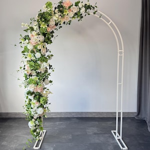 Könnte beinhalten: Weißer Metall-Hochzeitsbogen, geschmückt mit einem Blumenarrangement. Die Blumen sind weiß, rosa und grün. Der Bogen hat eine gebogene Form und einen rechteckigen Sockel.