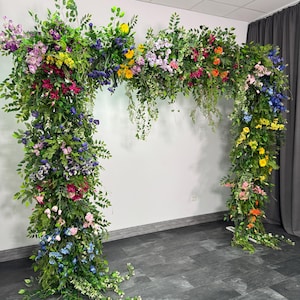 May include: A floral archway adorned with a vibrant array of colorful flowers and lush green foliage. The arch features a variety of blooms in shades of pink, blue, yellow, and orange, creating a visually appealing display. The arch is a decorative element.