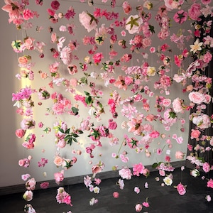 A display of pink and white flowers suspended from the ceiling. The flowers are of various types and sizes, creating a whimsical and romantic atmosphere. The flowers are arranged on strings, creating a curtain-like effect. Hanging flowers romantic decor, silk floating flower garland, floral party backdrop