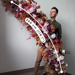 May include: A large floral arrangement, approximately 300 cm (118.1") long, featuring a cascade of burgundy, pink, and white flowers and foliage. The arrangement includes roses and other blooms, with a variety of textures and colours.