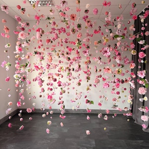 May include: A display of pink and light pink flowers suspended from the ceiling. The flowers are of various sizes and shapes, creating a whimsical and romantic atmosphere. The flowers are arranged in a way that they appear to be floating in the air.