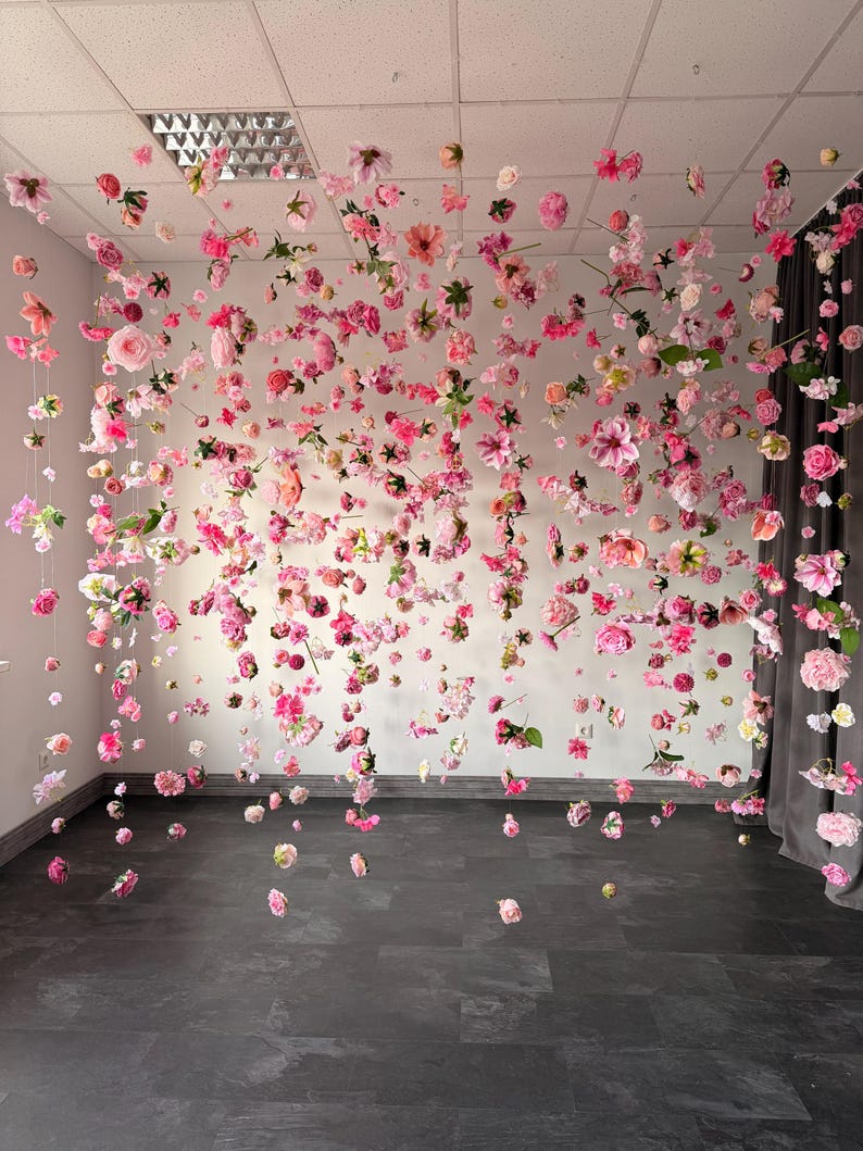 May include: A display of pink and light pink flowers suspended from the ceiling. The flowers are of various sizes and shapes, creating a whimsical and romantic atmosphere. The flowers are arranged in a way that they appear to be floating in the air.