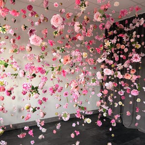 May include: A display of hanging pink and white flowers, including roses and other varieties, suspended from the ceiling. The flowers are arranged to create a visually appealing, immersive floral installation. The background is a neutral color.