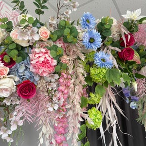 May include: A vibrant floral arrangement featuring a variety of flowers in shades of pink, blue, white, and green. The arrangement includes roses, hydrangeas, and cascading wisteria, creating a lush and colorful display.