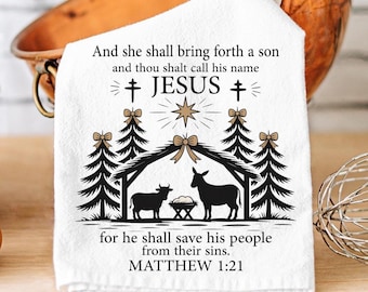 May include: White kitchen towel with a Nativity scene design. The design includes a star, trees, and silhouettes of animals. Text on the towel reads "And she shall bring forth a son...JESUS...for he shall save his people...MATTHEW 1:21."