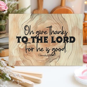 May include: A wooden sign featuring the words "Oh give thanks TO THE LORD For he is good." in black. The background has a wood grain pattern in brown and beige. The Bible verse "1 Chronicles 16:34" is also included on the sign.