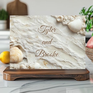 May include: A decorative wooden sign with the names "Tyler and Brooke" in elegant script. The sign features a textured, off-white background with seashells, mounted on a dark wooden base.