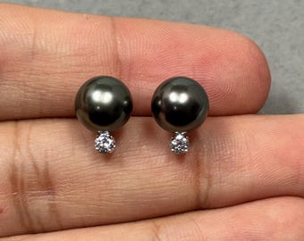 May include: A pair of dark grey pearl stud earrings with small, sparkling white diamond accents. The earrings are round and have a polished, reflective surface. The diamonds are set in a cluster design.