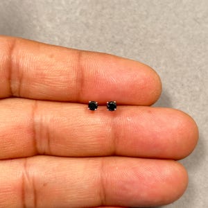 May include: A pair of small, round black stud earrings. The earrings are set in a silver-colored metal and are displayed on a neutral background.