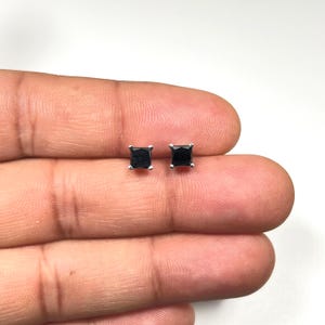 Puede incluir: Un par de pendientes de botón cuadrados de piedra preciosa negra. Los pendientes están engastados en un metal color plata. Las piedras preciosas son de color negro intenso y tienen forma cuadrada. Los pendientes son pequeños y delicados.