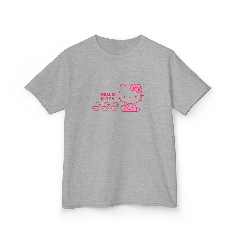 Puede incluir: Camiseta gris con un dise&ntilde;o rosa de Hello Kitty y tres patitos. El texto "Hello Kitty" est&aacute; encima del personaje. El dise&ntilde;o est&aacute; centrado en la parte delantera de la camiseta.