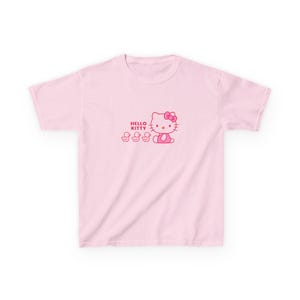 Puede incluir: Camiseta rosa claro con un dise&ntilde;o de Hello Kitty. El dise&ntilde;o incluye el texto "HELLO KITTY", Hello Kitty y tres patitos, todos en rosa. La camiseta tiene cuello redondo y mangas cortas.