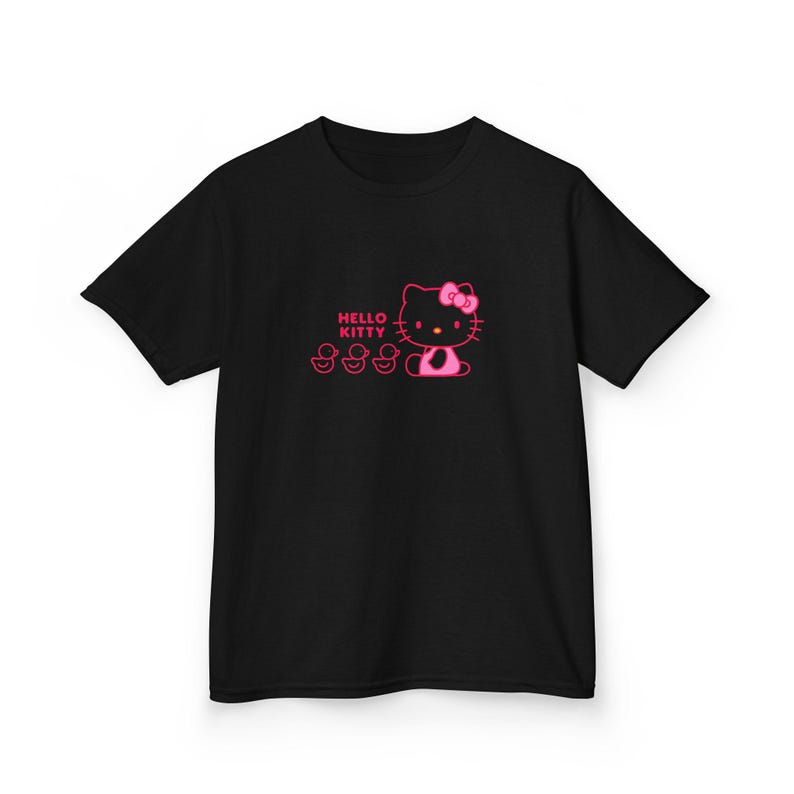 Puede incluir: Camiseta negra con un dise&ntilde;o rosa de Hello Kitty con un lazo y tres patitos. Las palabras "Hello Kitty" est&aacute;n impresas encima del personaje. El dise&ntilde;o est&aacute; centrado en la parte delantera de la camiseta.
