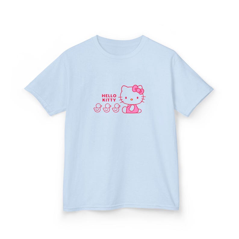 Puede incluir: Camiseta azul claro con un dise&ntilde;o rosa de Hello Kitty. El dise&ntilde;o incluye las palabras "Hello Kitty" y tres patitos. El gr&aacute;fico est&aacute; centrado en la parte delantera de la camiseta. La camiseta es de material suave.