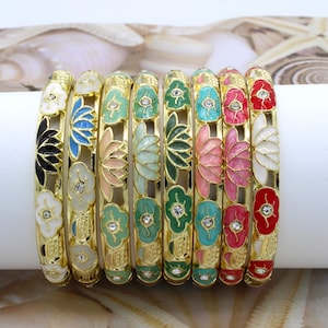May include: A collection of eight gold-toned bangles, each adorned with a different color floral design. The flowers are painted in various colors, including white, black, blue, pink, green, and red, and are accented with small, clear gemstones. The bangles are displayed on a white surface.