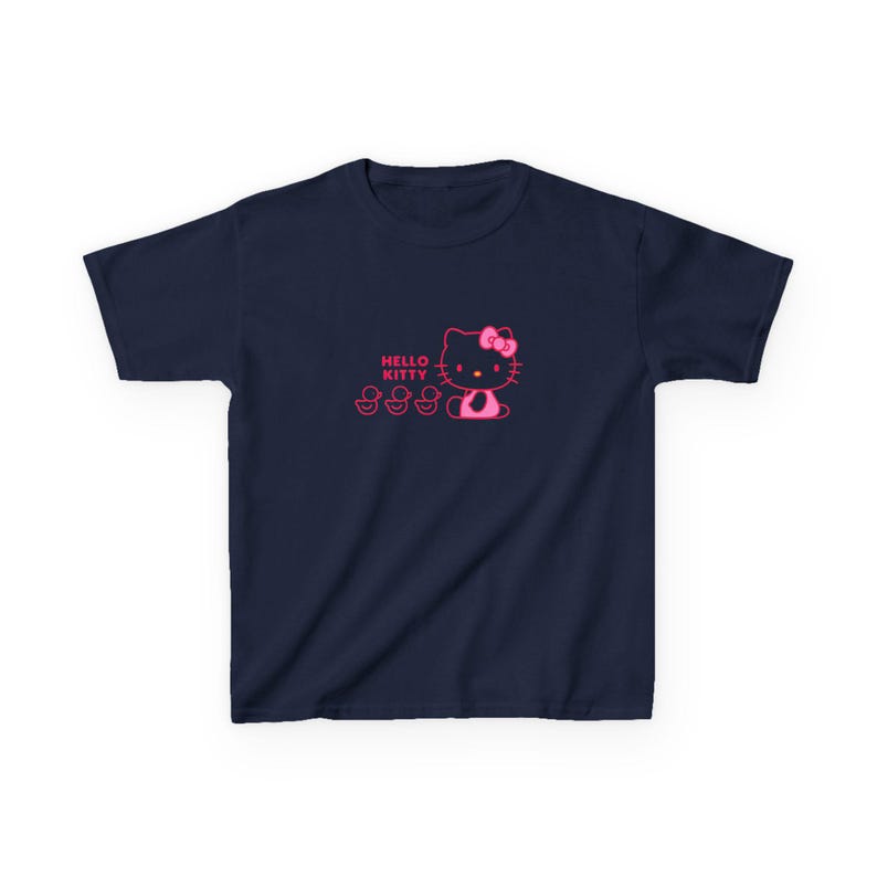 Puede incluir: Camiseta azul marino con un dise&ntilde;o rosa de Hello Kitty, que incluye un lazo y tres patitos. Las palabras "Hello Kitty" est&aacute;n impresas encima del personaje. La camiseta est&aacute; hecha de un material suave.