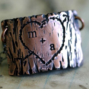 Op de afbeelding: Een koperen ketting met een hartvormige hanger. De hanger is getextureerd om eruit te zien als boomschors en heeft de initialen "M + A" gegraveerd in het hart.