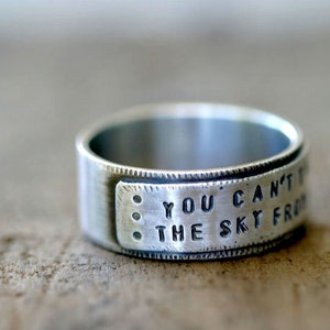 May include: A silver ring with the inscription "You can't touch the sky from here".