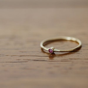 Op de afbeelding: Een eenvoudige gouden ring met een kleine, ronde, rode edelsteen.
